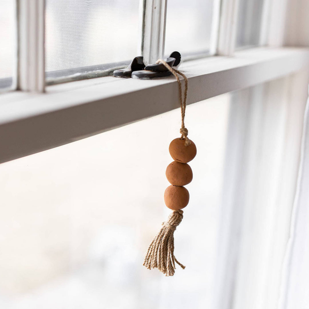 Decorative hanging with wooden beads and tassel in front of a window